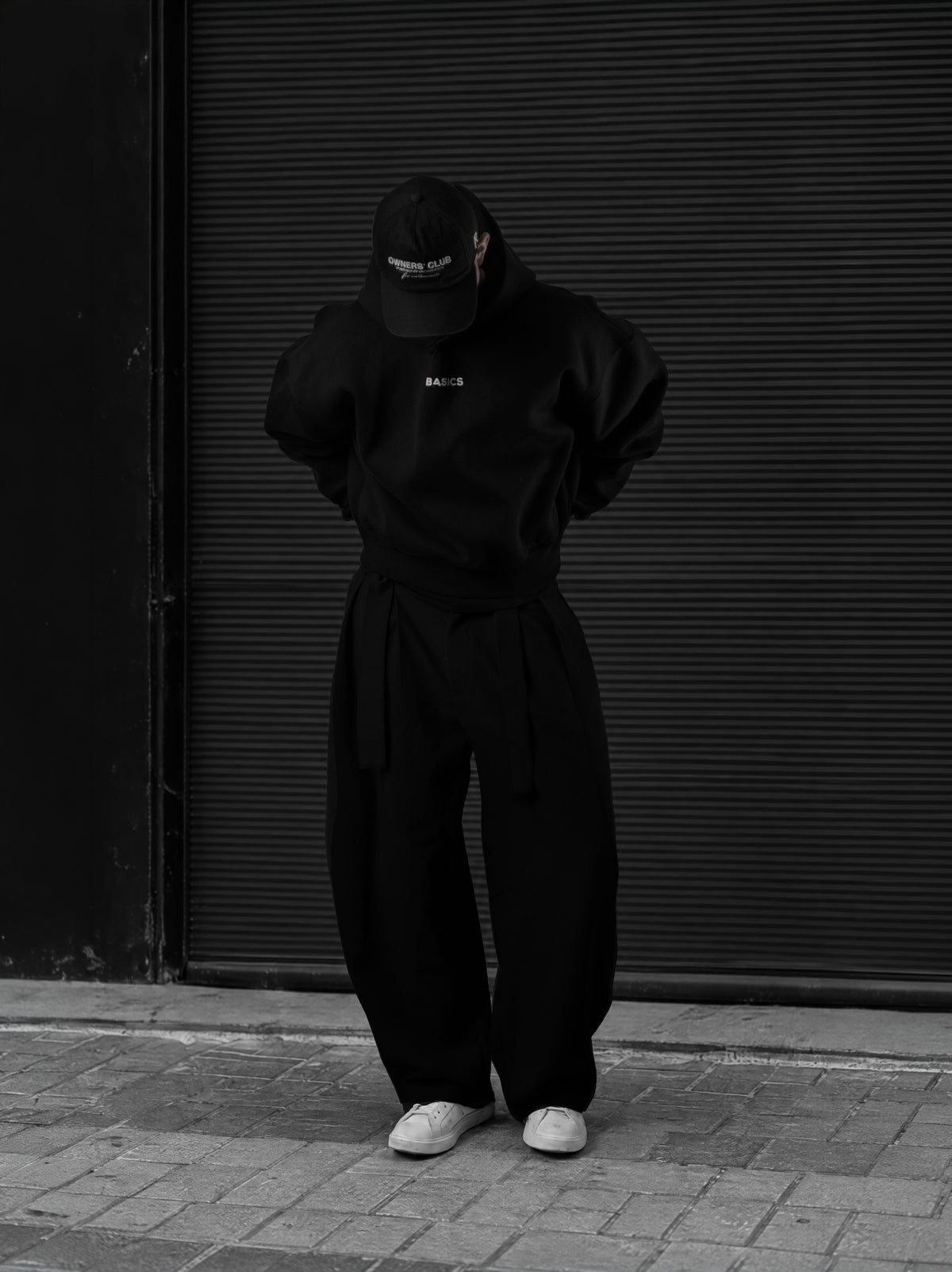 The Founders Hoodie negro en la calle, con la cabeza baja